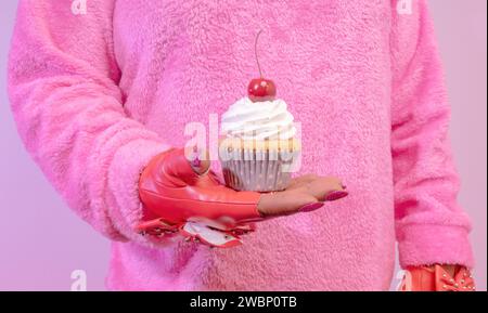 Una mujer afroamericana diversa que lleva guantes de moda rojos tachonados y sosteniendo Un cupcake esmerilado de vainilla con una cereza en la parte superior Foto de stock