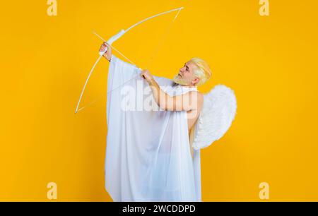 Cupido masculino en alas de ángel en el día de San Valentín con arco y flecha. Dios de amor. San Valentín ángel disparando flecha de amor. Hombre barbudo sonriente en ángel Foto de stock