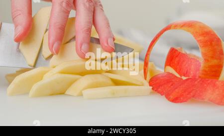 Manos de mujer cortando manzanas peladas en una tabla de cortar blanca, receta de pastel de manzana Foto de stock