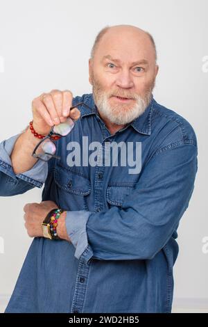 Retrato de un hombre de pelo gris indignado en una camisa de mezclilla sobre un fondo blanco. Abuelo barbudo del tipo europeo. Foto de stock