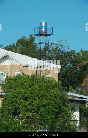 Tanque de agua de acero inoxidable en la torre para el almacenamiento de agua utilizado en hogares y fuentes de agua cuando el agua no está disponible. El fondo es un techo de la casa y. Foto de stock