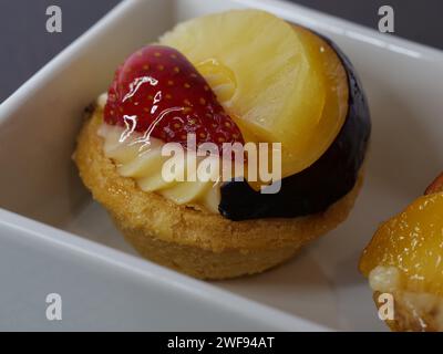 Una variedad de deliciosos postres bellamente dispuestos en un plato blanco prístino, acompañado de una fruta vibrante y suculenta Foto de stock