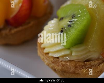 Una variedad de deliciosos postres bellamente dispuestos en un plato blanco prístino, acompañado de una fruta vibrante y suculenta Foto de stock