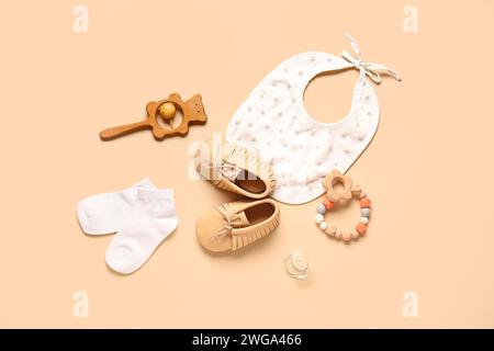 Zapatos de bebé con estilo con babero, sonajeros y calcetines sobre fondo beige Foto de stock