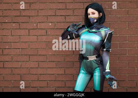 Una cosplayer femenina en un traje de acción verde contra una pared de ladrillo Foto de stock