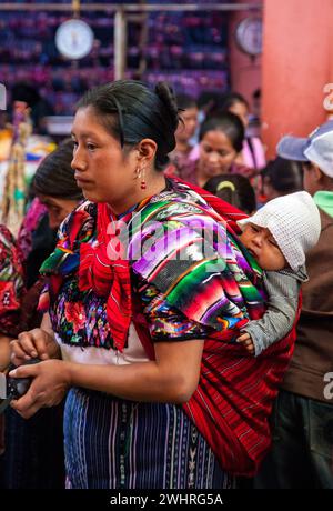 Chichicastenango, Guatemala. Quiche (Kiche, K'iche') de la Mujer con el bebé en la espalda en el mercado interior, la mañana del domingo. Foto de stock