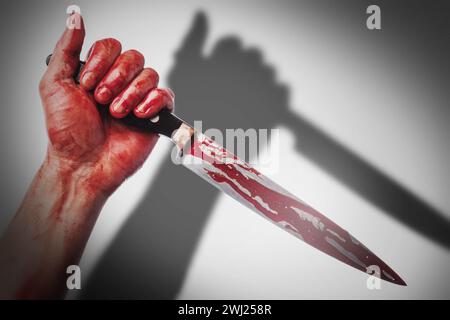 Mano masculina con un cuchillo en manchas de sangre echando sombra sobre fondo blanco Foto de stock