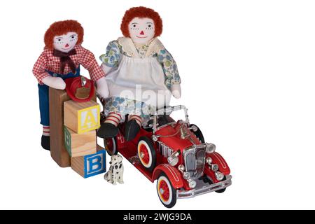 Muñecas de trapo hechas a mano, Raggedy Ann y Andy colocados entre juguetes, bloques, motor de bomberos, perrito, sombrero de bombero, juguetes viejos y nuevos en madera y metal. Aislado Foto de stock