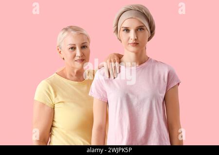 Mujer joven después de la quimioterapia con su madre sobre fondo rosa. Concepto de cáncer de estómago Foto de stock