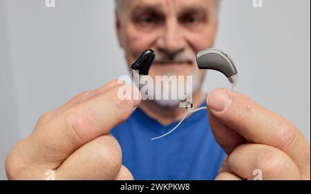 El hombre mayor con problemas auditivos elige entre el audífono detrás del oído y el audífono en el oído manteniéndolos frente a ella. Audífonos A Foto de stock