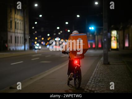 Dresde, Alemania. 06 de marzo de 2024. Un servicio de mensajería de bicicletas del servicio de entrega 'Lieferando' se monta a lo largo de un carril bici por la noche. Crédito: Robert Michael/dpa/Alamy Live News Foto de stock