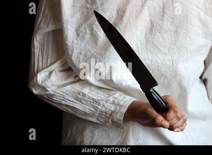 Mujer con blusa blanca sosteniendo un cuchillo. Concepto de violencia doméstica. Foto de stock