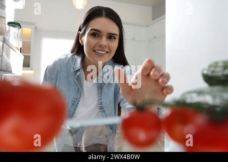 Mujer joven cerca del refrigerador en la cocina, vista desde el interior Foto de stock