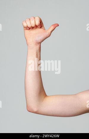 Adulto joven que realiza la letra de lenguaje de señas americano L contra un fondo llano Foto de stock