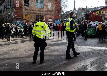 Policía danesa patrullando en la calle Pusher en Freetown Christiania durante un día de acción el sábado 6 de abril de 2024. En una reunión en Christiania en marzo, se decidió que la llamada calle Pusher en el famoso barrio de Copenhague debía ser excavada durante un llamado día de acción el 6 de abril. Está previsto que Christianitter, ayudado por obreros, cava la calle. Personas de fuera de Christiania son bienvenidas a participar según lo informado por el portavoz de Christiania. Al desenterrar la calle, los habitantes de Christiania esperan impedir que las bandas criminales continúen su tráfico de drogas en la ubicación Co Foto de stock