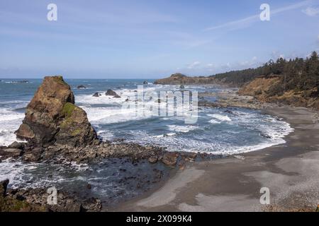 Una playa rocosa con una gran roca en primer plano y un cuerpo de agua en el fondo. La escena es tranquila y pacífica, con las olas soltando suavemente Foto de stock