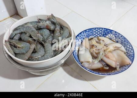 Unos calamares crudos y camarones en cuencos en una mesa de cocina Foto de stock