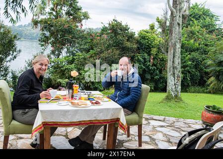 Una pareja desayuna cómodamente en los jardines del hotel situado en el centro del lago Bunyonyi en el sur de Uganda Foto de stock