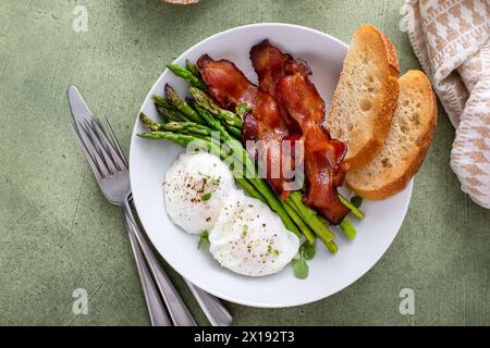 Huevos escalfados con tocino y espárragos para el desayuno servido con tostadas Foto de stock