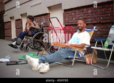 Hombre sin hogar y paralizado a una mujer sentada sobre la acera en el calor del verano en Upper Manhattan la ciudad de Nueva York. Foto de stock