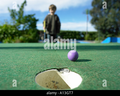 Joven Getting abajo para comprobar la mentira de un disparo en el crazy golf putter y con una pequeña bola púrpura Foto de stock