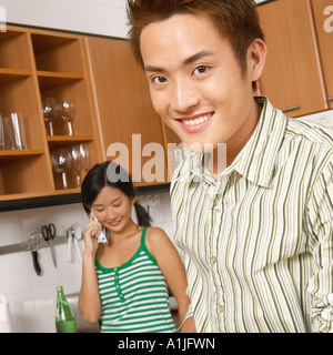 Retrato de un joven cortando verduras en la cocina con una mujer joven hablando por un teléfono móvil en el fondo