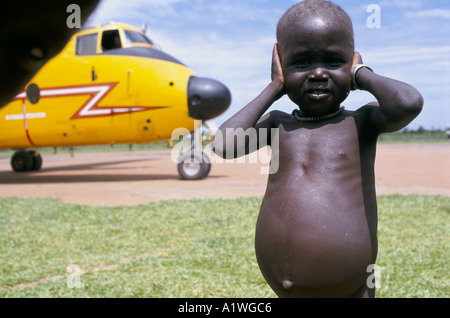 Sudán del sur de agosto de 1998 el hambre. Los niños malnutridos SHIELDS SUS OÍDOS DE LOS RUIDOS DE UN AVIÓN entregando ayuda alimentaria Foto de stock