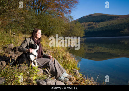 Mujer sentada con el perro en el otoño, Talybont depósito, Brecon Beacons NP, Gales, GB Foto de stock