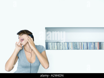 Mujer escuchando auriculares, estante de cds en segundo plano.