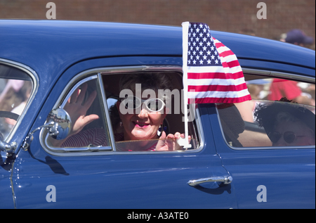 Mujer de más edad que viajaba en un automóvil Hudson vintage tejiendo una bandera americana durante un desfile del 4 de julio Foto de stock
