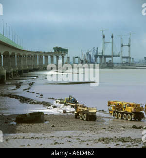 Vehículos contratistas que conducen a través del río en marea baja con materiales de construcción para el Puente Príncipe de Gales o cruce de Severn segundo Foto de stock