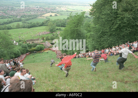 Valientes competidores chase giant Double Gloucester quesos Coopers colina abajo en los Cotswolds Foto de stock