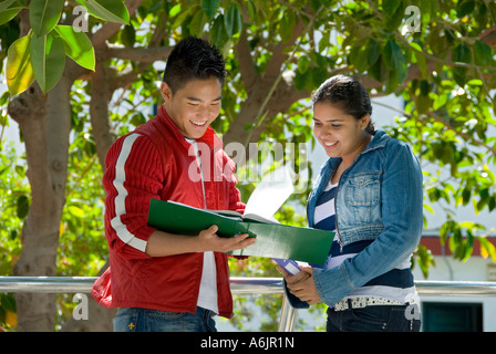 Estudiantes al aire libre estudiar relajado Asia Oriental dos estudiantes adolescentes mayores sonriendo comparan notas de estudio fuera en el patio de recreo del jardín escolar Foto de stock