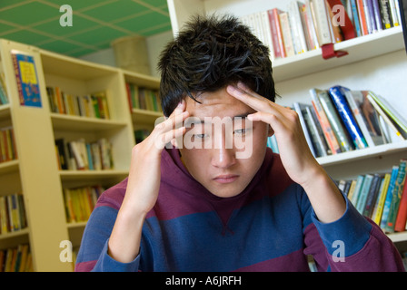 Muchacho adolescente coreano orientales bajo la presión del tiempo del examen se concentra intensamente en su examen de la biblioteca de la escuela de estudios Foto de stock