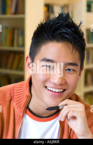 Adolescente coreano 15-17 años estudiante de escuela superior oriental moderno guapo muchacho adolescente sonriendo, relajarse durante sus estudios en la biblioteca escolar Foto de stock