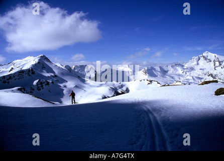 La pequeña figura de un esquí alpinista haciendo su propia pista en el alto paisaje alpino de Tessin, Suiza Foto de stock