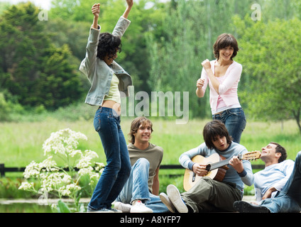 Grupo de amigos en el exterior, jóvenes mujeres bailando mientras toca la guitarra joven