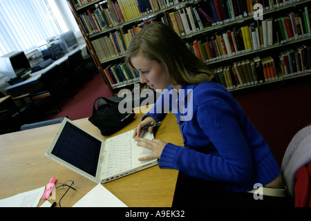 Joven estudiante trabajando estudiando en una biblioteca utilizando un ordenador portátil en sus estudios Foto de stock