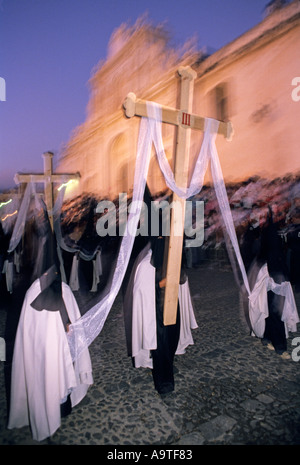 Manifestantes en procesión de Semana Santa llevan cruces y vestir trajes con capucha en frente de la Iglesia Católica Antigua Guatemala Foto de stock