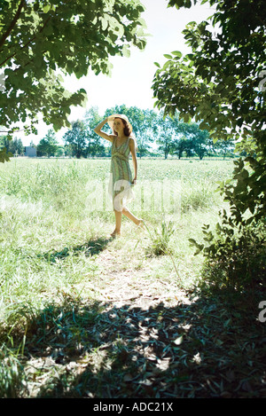 Joven mujer vistiendo sundress y sombrero para el sol, caminar por el campo