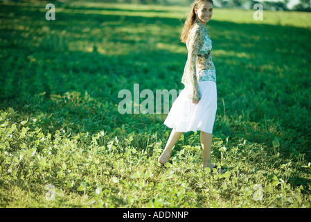 Mujer joven caminando por el campo, sonriendo a la cámara