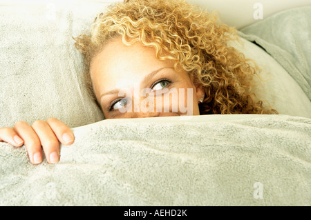 Mujer asoma desde debajo de cubiertas en la cama Foto de stock