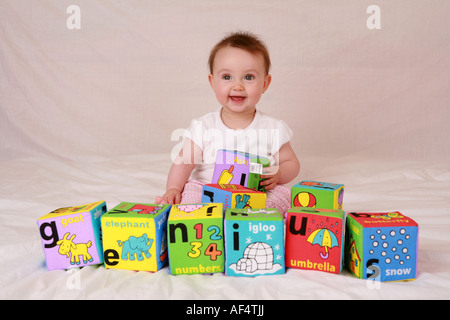 Feliz sonriente genio inteligente smart bebé recién nacido niño sentado jugando con carta de bloques de creación de word ortografía GENIO Foto de stock