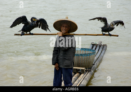 Retrato de un pescador sosteniendo un polo con dos cormoranes en ambos lados del río Li, Yangshuo, Guangxi, China. Foto de stock