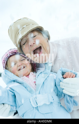 Mujer mayor y su nieta mejilla a la mejilla en nieve, sonriendo, con los ojos cerrados
