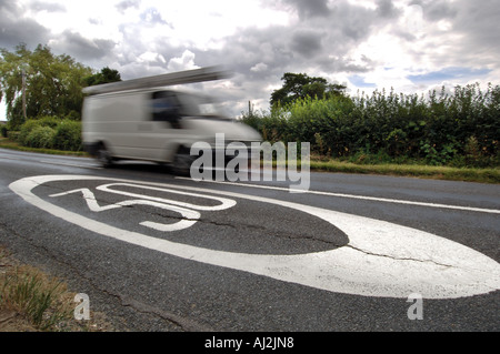 Una furgoneta blanca borrosa silbe pasado un límite de 30 mph signo pintado en una carretera rural. Foto de stock