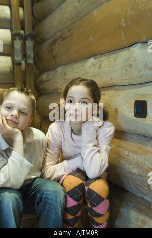 Preadolescentes chico y chica sentada al lado de la otra, mirando hacia afuera del bastidor Foto de stock