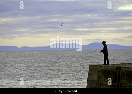 Pesca en el Moray Firth desde el muro del puerto en Portknockie, con las montañas de la Isla Negra en la distancia Foto de stock