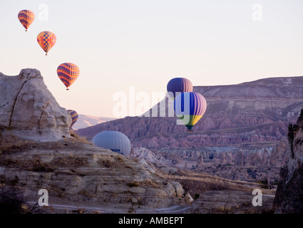 Arriba arriba y lejos de siete colores de lanzamiento de globos de aire caliente en el amanecer Cappadocian rocas púrpura detrás