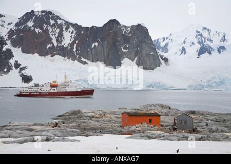 Un crucero Antártico se asienta en el ancla detrás de una colonia de pingüinos Gentoo en la Isla Petermann Foto de stock